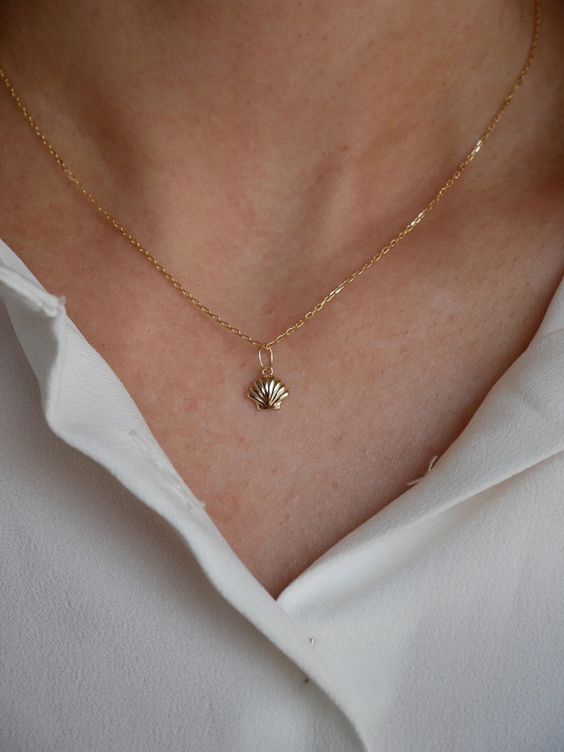 May include: A gold chain necklace with a small seashell pendant.