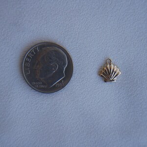 May include: A gold-colored seashell charm pendant. The charm is about the size of a dime.