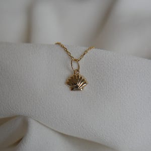 May include: A gold chain necklace with a small, detailed seashell pendant.