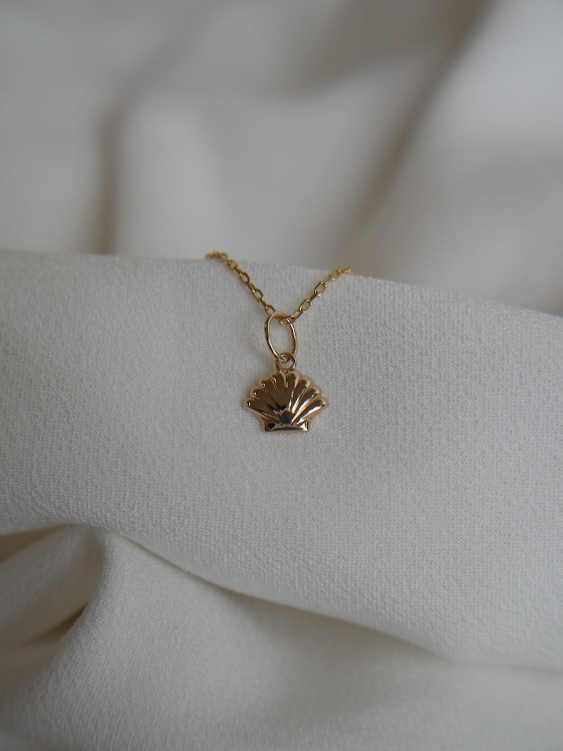 May include: A gold chain necklace with a small, detailed seashell pendant.