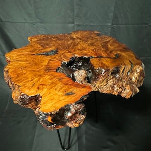 Puede incluir: Una mesa de café de madera rústica con una tapa de borde vivo y patas de horquilla negras. La madera tiene una forma natural y orgánica y un color marrón cálido y rico.