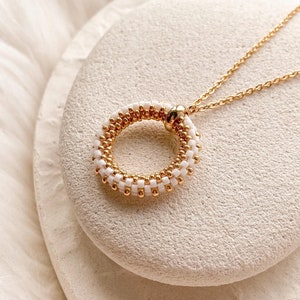 Peut inclure: Un collier en chaîne dorée avec un pendentif rond en perles blanches et dorées.