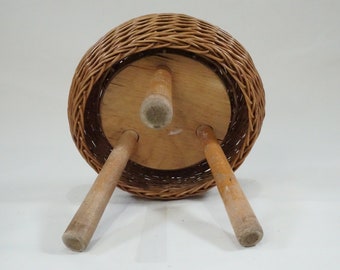 May include: A round wicker stool with a wooden top and three wooden legs. The stool is brown and has a natural finish.