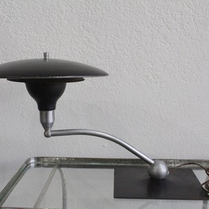 May include: A black and silver mid-century modern desk lamp with a curved arm and a round base. The lampshade is a flat disc.