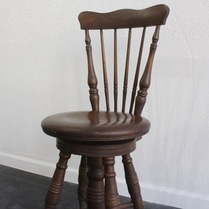 Puede incluir: Una silla giratoria de madera marrón oscuro con respaldo de huso torneado y patas torneadas.