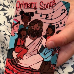 Może przedstawiać: Okładka książki dla dzieci zatytułowana "Primary Songs" z ilustracją dzieci i mężczyzny z brodą, otoczonych nutami. Okładka ma różowe tło i czerwoną obwódkę.