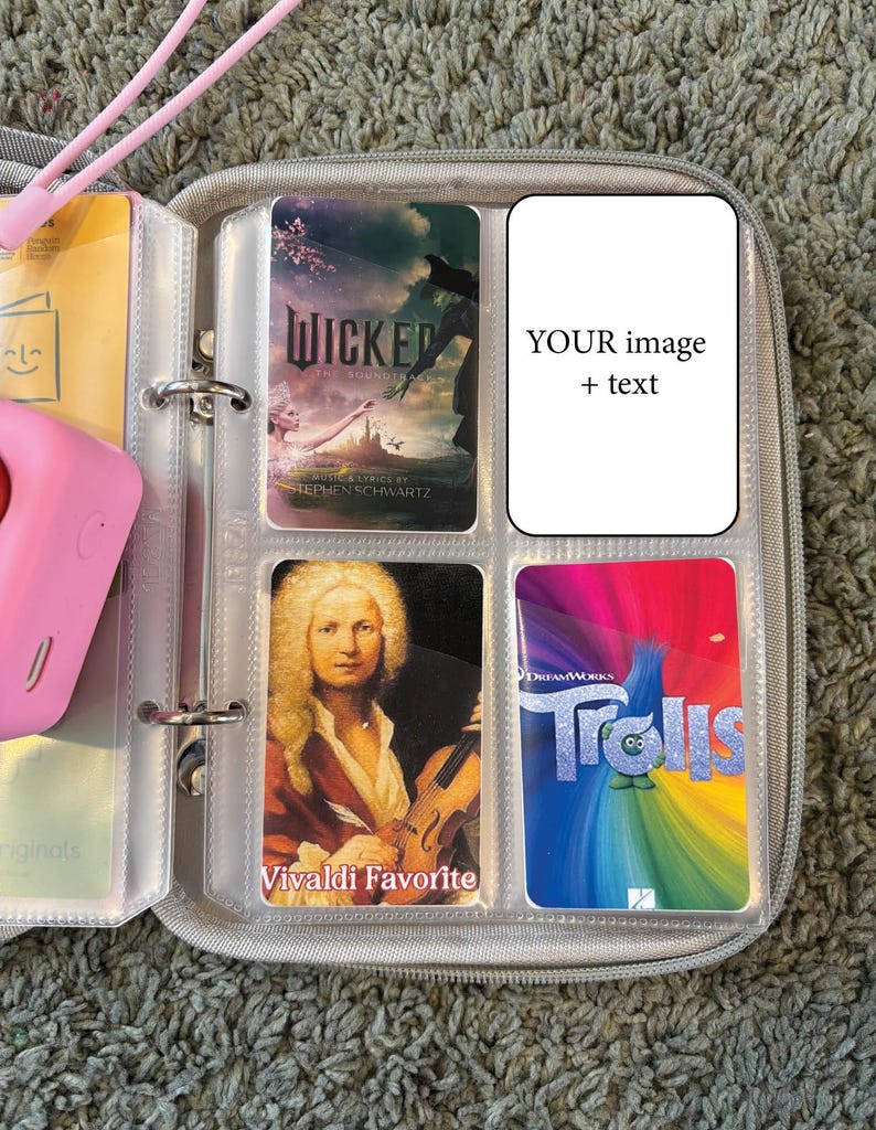 May include: A clear plastic binder containing a selection of colourful cards. The cards feature images of a musical score, a portrait of a man, a movie poster, and a musical play. The binder has a ring mechanism for holding the cards.