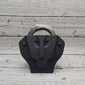 May include: A black leather handcuff holster with a silver handcuff inside. The holster has a textured surface and two small screws on the side.