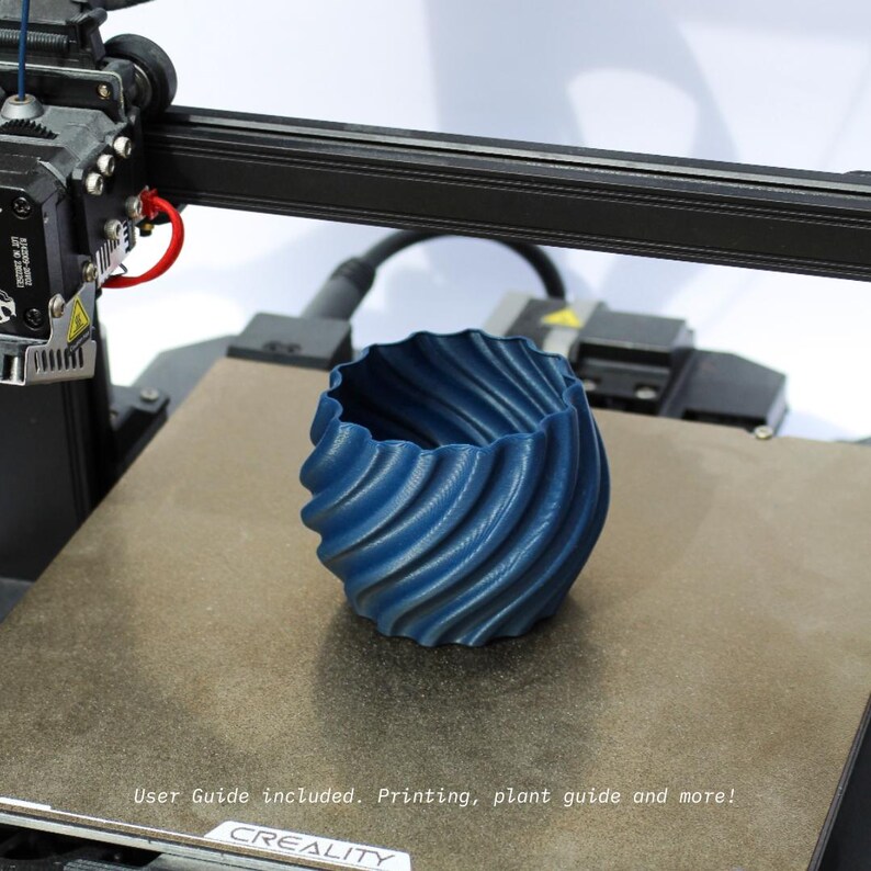 Navy blue 3D printed plant pot sitting on a 3D printer printing bed, photographed on a white background.