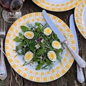 Peut inclure: Mise en place avec des assiettes blanches bordées de motifs géométriques jaunes. Un verre de vin rouge, des couverts et une assiette de salade aux œufs coupés sont également présents. Les assiettes mesurent environ 25 cm de diamètre.