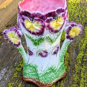 Könnte beinhalten: Eine weiße Keramikvase mit rosafarbenem Innenraum und einem Blumendesign. Die Vase zeigt violette und gelbe Stiefmütterchen mit grünen Blättern. Die Vase hat zwei Henkel und einen gewellten Rand.
