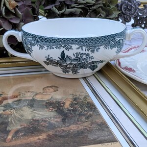 K&ouml;nnte beinhalten: Eine wei&szlig;e Suppensch&uuml;ssel aus Keramik mit einem blauen und gr&uuml;nen Blumenmuster. Die Sch&uuml;ssel hat zwei Henkel und einen gewellten Rand.