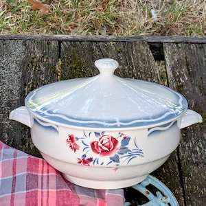 Peut inclure: Une soupière en céramique blanche avec couvercle, bordure bleue et motif floral avec roses rouges et feuilles bleues. La soupière a deux poignées et un bouton sur le couvercle. Un article de cuisine vintage.