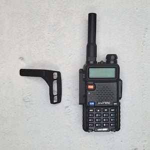 May include: A black handheld two-way radio with a black antenna, a black keypad, and a blue LCD screen. The radio has the text "BAOFENG" and "UV-5R" printed on it.