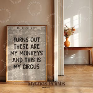 May include: A framed print featuring the text "TURNS OUT THESE ARE MY MONKEYS AND THIS IS MY CIRCUS" in black on a newspaper background. The print is in a wooden frame and is displayed on a wooden floor.
