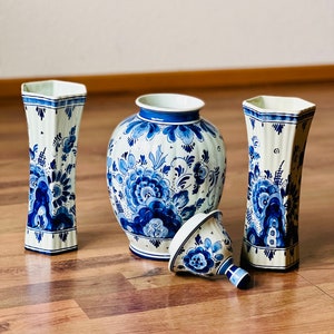 May include: A set of four blue and white Delftware vases with floral designs. The vases are arranged on a wooden surface.