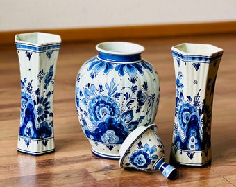 May include: A set of four blue and white Delftware vases with floral designs. The vases are arranged on a wooden surface.