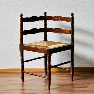 Op de afbeelding: Een vintage houten stoel met een geweven strooien zitting. De stoel heeft een donkerbruine afwerking, gesneden details op de rugleuning en gedraaide poten. De afmetingen van de stoel zijn ongeveer 46 cm breed, 46 cm diep en 91 cm hoog.