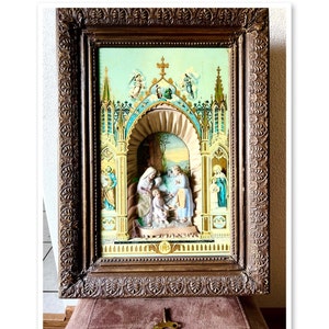 May include: A vintage framed religious artwork with a 3D scene of Mary, Joseph, and baby Jesus. The scene is set in a cathedral with a blue and green background. The frame is ornate and has a gold finish.