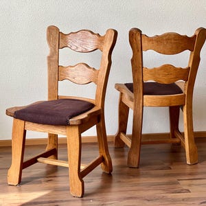 May include: Two wooden chairs with brown upholstered seats. The chairs have a simple design with a curved back and four legs.