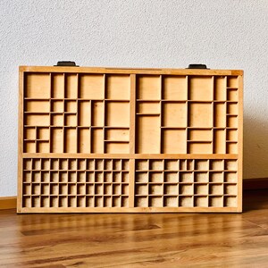 May include: A wooden printing tray with multiple compartments of various sizes. The tray is made of light brown wood and has a rectangular shape.