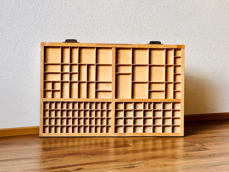 May include: A wooden printing tray with multiple compartments of various sizes. The tray is made of light brown wood and has a rectangular shape.