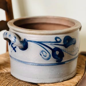 Op de afbeelding: Een grote, grijze steengoed pot met een blauw-wit bloemenmotief. De pot heeft twee handvatten en een brede opening.