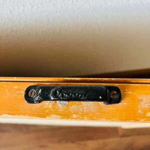 May include: Close-up of a black metal handle with the word "Genuine" embossed on it. The handle is attached to a wooden surface.