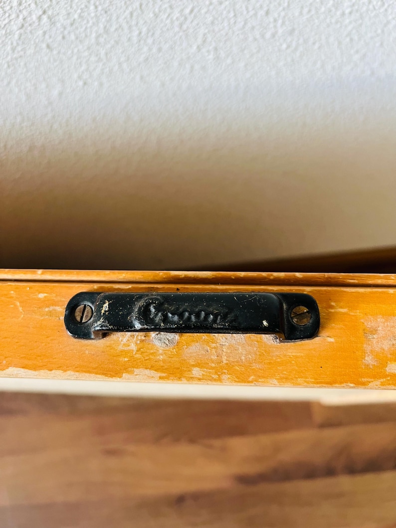 May include: Close-up of a black metal handle with the word "Genuine" embossed on it. The handle is attached to a wooden surface.