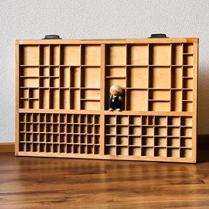 May include: A wooden drawer organizer with multiple compartments. The organizer is made of light brown wood and has a natural finish. The compartments are arranged in a grid pattern and are of varying sizes. A small wooden figurine is placed in one of the compartments.