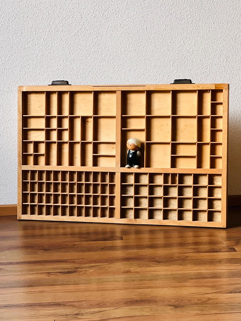 May include: A wooden drawer organizer with multiple compartments. The organizer is made of light brown wood and has a natural finish. The compartments are arranged in a grid pattern and are of varying sizes. A small wooden figurine is placed in one of the compartments.