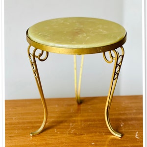 May include: A small, round, gold-colored metal table with a green marble top. The table has three legs with ornate designs.