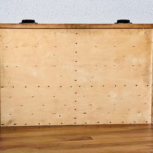 May include: A wooden storage box with a light brown finish and black metal hinges. The box has a plain surface with a pattern of small holes.