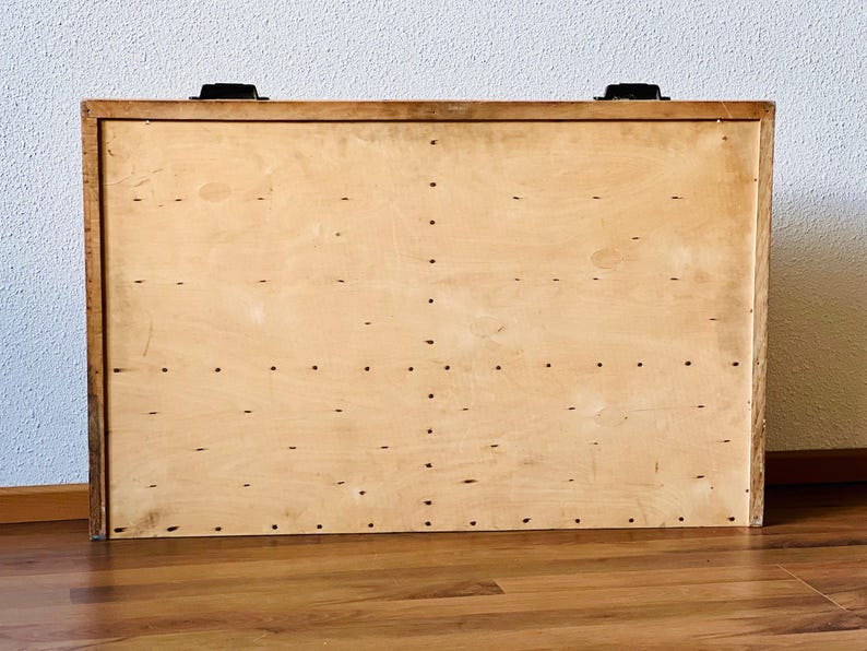 May include: A wooden storage box with a light brown finish and black metal hinges. The box has a plain surface with a pattern of small holes.