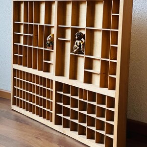 May include: A wooden printer's tray with multiple compartments. The tray is made of light brown wood and has a rectangular shape. The tray is empty.