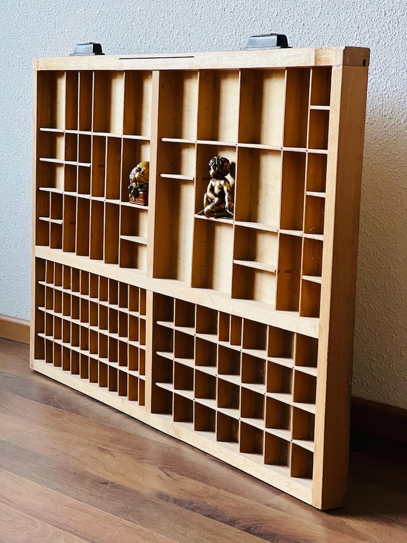 May include: A wooden printer's tray with multiple compartments. The tray is made of light brown wood and has a rectangular shape. The tray is empty.