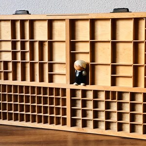 May include: A wooden storage box with multiple compartments, featuring a small figurine of a person standing in one of the compartments.