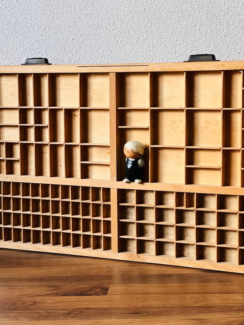 May include: A wooden storage box with multiple compartments, featuring a small figurine of a person standing in one of the compartments.