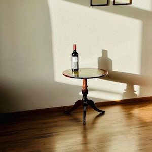 May include: A wooden side table with a round top and three legs. A bottle of red wine is on the table.