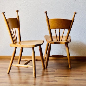 Könnte beinhalten: Zwei Holzstühle mit schlichtem Design. Die Stühle haben eine hellbraune Oberfläche und sind aus massivem Holz gefertigt. Die Stühle stehen in einem Raum mit einer weißen Wand und einem Holzboden.