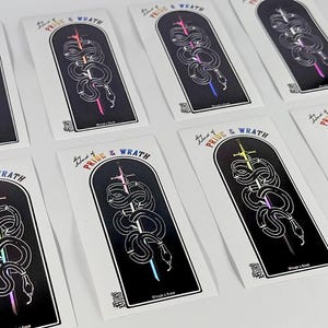 May include: A collection of stickers featuring a black and white design of a snake coiled around a sword. The stickers have a rainbow gradient and the text "Pride & Wrath". The stickers are on a white background.