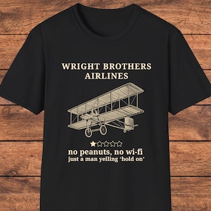 May include: Black t-shirt featuring the text "WRIGHT BROTHERS AIRLINES" above a sepia-toned illustration of a biplane. Below the plane, the text reads "no peanuts, no wi-fi just a man yelling 'hold on'".