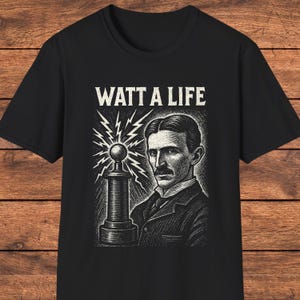 Könnte beinhalten: Ein schwarzes Kurzarm-T-Shirt mit einem weißen Grafikdruck von Nikola Tesla neben einer Tesla-Spule. Über der Illustration ist der Text WATT A LIFE in einer fetten, abgenutzten weißen Schriftart gedruckt. Das Design nutzt Schraffuren.