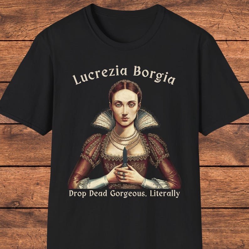 May include: A black short-sleeved t-shirt featuring a graphic of Lucrezia Borgia in a red dress with a high collar and pearl necklaces. She holds a small dagger. The text reads Lucrezia Borgia above and Drop Dead Gorgeous. Literally below.