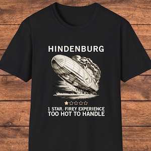 May include: A black t-shirt featuring a graphic of the Hindenburg airship in flames. Above the airship is the text HINDENBURG. Below the graphic is a single gold star followed by four empty stars, and the text 1 STAR. FIREY EXPERIENCE TOO HOT TO HANDLE.