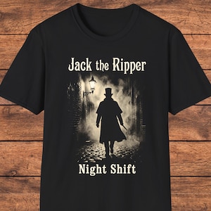 May include: A black short-sleeved t-shirt featuring a graphic print of a silhouette in a top hat and long coat walking down a foggy cobblestone alleyway under a street lamp, with the text Jack the Ripper above and Night Shift below the image.