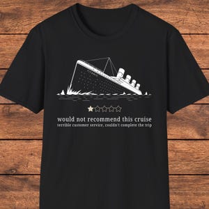 Pode incluir: Uma t-shirt preta de manga curta com um gráfico de linhas brancas do naufrágio do Titanic. Abaixo do navio há uma estrela preenchida de cinco, com o texto: would not recommend this cruise, terrible customer service, couldn't complete the trip.