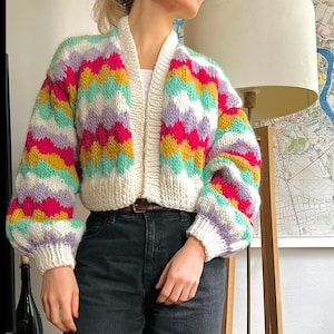 May include: A colorful striped cardigan with a white background and long sleeves. The cardigan has a V-neck and is cropped.