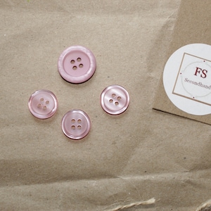Könnte beinhalten: Vier rosa Knöpfe mit jeweils vier Löchern auf braunem Papieruntergrund. Ein weißer Kreis mit dem Text "FS Secondhand" befindet sich oben rechts.