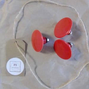 Könnte beinhalten: Drei rote, ovale Schrankknöpfe mit silbernen Beschlägen liegen auf braunem Papier. Ein Stück Schnur und ein kleines Etikett mit den Buchstaben "FS" und dem Wort "secondhand" sind ebenfalls vorhanden.